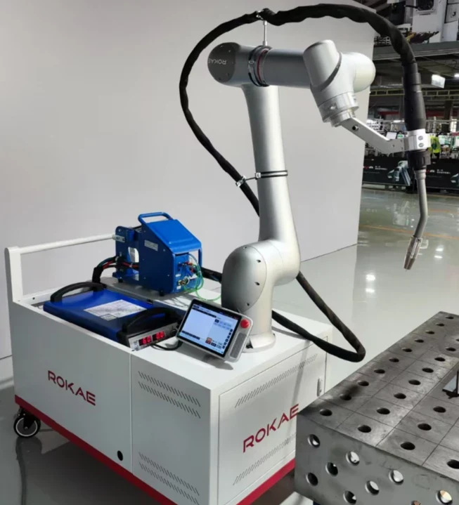 ROKAE xMate collaborative robot with a welding torch on a mobile welding cart, beside a welding table